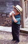 Amish toddler drinks near wooden bridge by Dennis L. Hughes