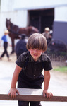 Amish boy leaning over fence by Dennis L. Hughes
