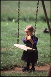Amish girl eating behind swing by Dennis L. Hughes
