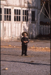 Young boy standing in front of stables by Dennis L. Hughes